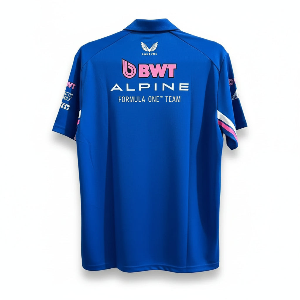 A royal blue short-sleeve team shirt shown from the back, featuring 'BWT ALPINE FORMULA ONE TEAM' in white and pink text, with a wing logo at the neck, hanging against a white decorative screen.