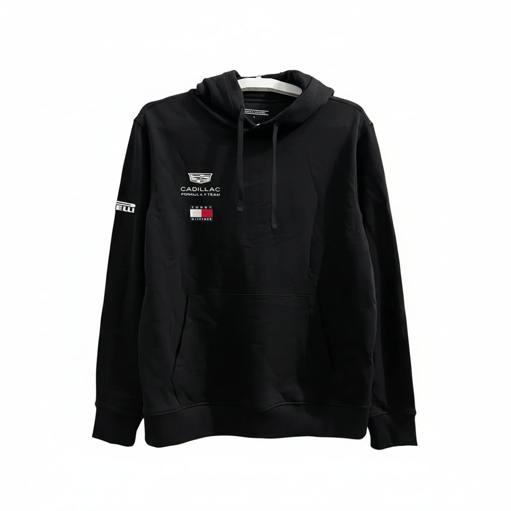 A black pullover hoodie featuring Cadillac F1 Team branding on the left chest and Pirelli on the right sleeve, hanging against a white decorative screen.