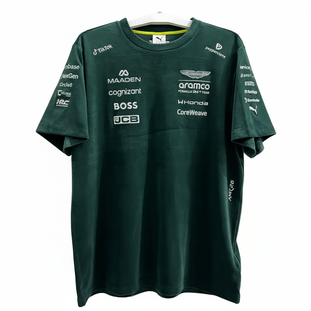 A dark green Mercedes-AMG F1 team t-shirt with various sponsor logos printed on the front, hanging on a white hanger against a decorative white screen.