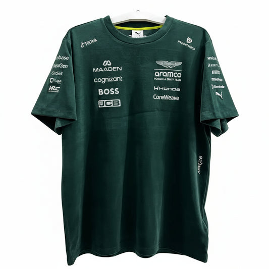 A dark green Mercedes-AMG F1 team t-shirt with various sponsor logos printed on the front, hanging on a white hanger against a decorative white screen.