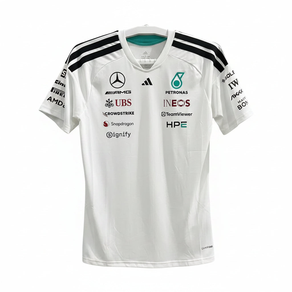 A white Mercedes-AMG Petronas Formula 1 racing jersey with black shoulder stripes and multiple sponsor logos, hanging against a decorative black-and-white patterned background.