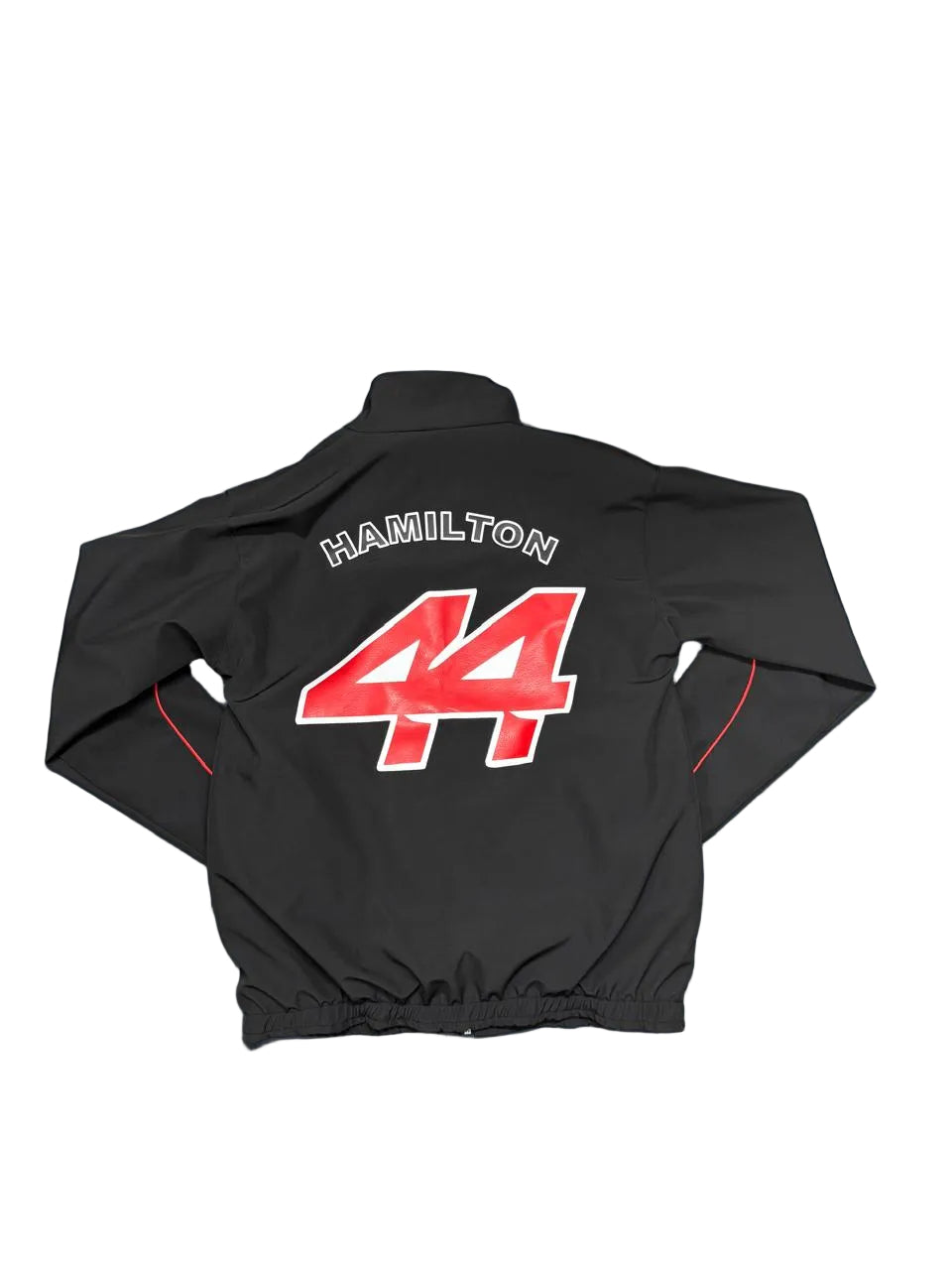 A black zip-up jacket laid flat on a blue sheet, showing the back with 'HAMILTON' and the number '44' in red and white. Bare feet are visible at the bottom edge, and a room floor and storage items are in the background.