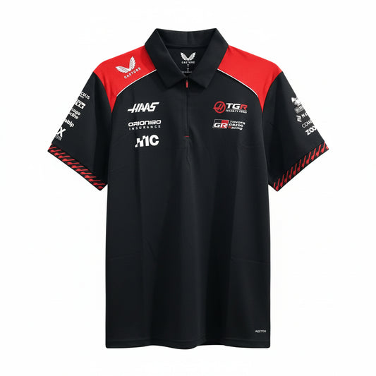 A black and red short-sleeve collared team polo shirt with multiple sponsor logos, hanging on a white hanger against a decorative white wall with leaf-shaped cutouts.