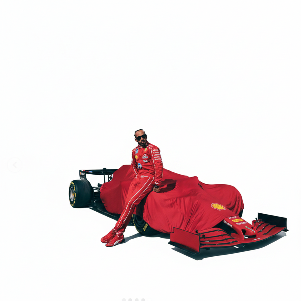 A man in a red racing suit and matching red shoes leans against a red-covered race car in a pit area, with a red wall and dark asphalt in the background.