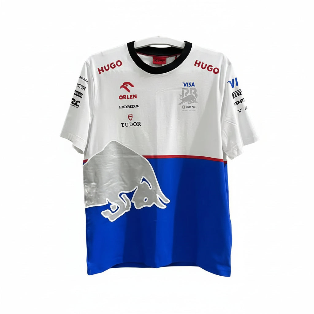 A white and blue Red Bull Racing t-shirt with sponsor logos, featuring a large silver bull graphic on the lower front, hanging against a decorative white screen.
