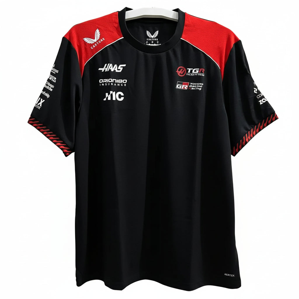 A black and red short-sleeve athletic jersey with multiple sponsor logos, hanging on a white hanger against a decorative white wall with leaf-shaped cutouts.